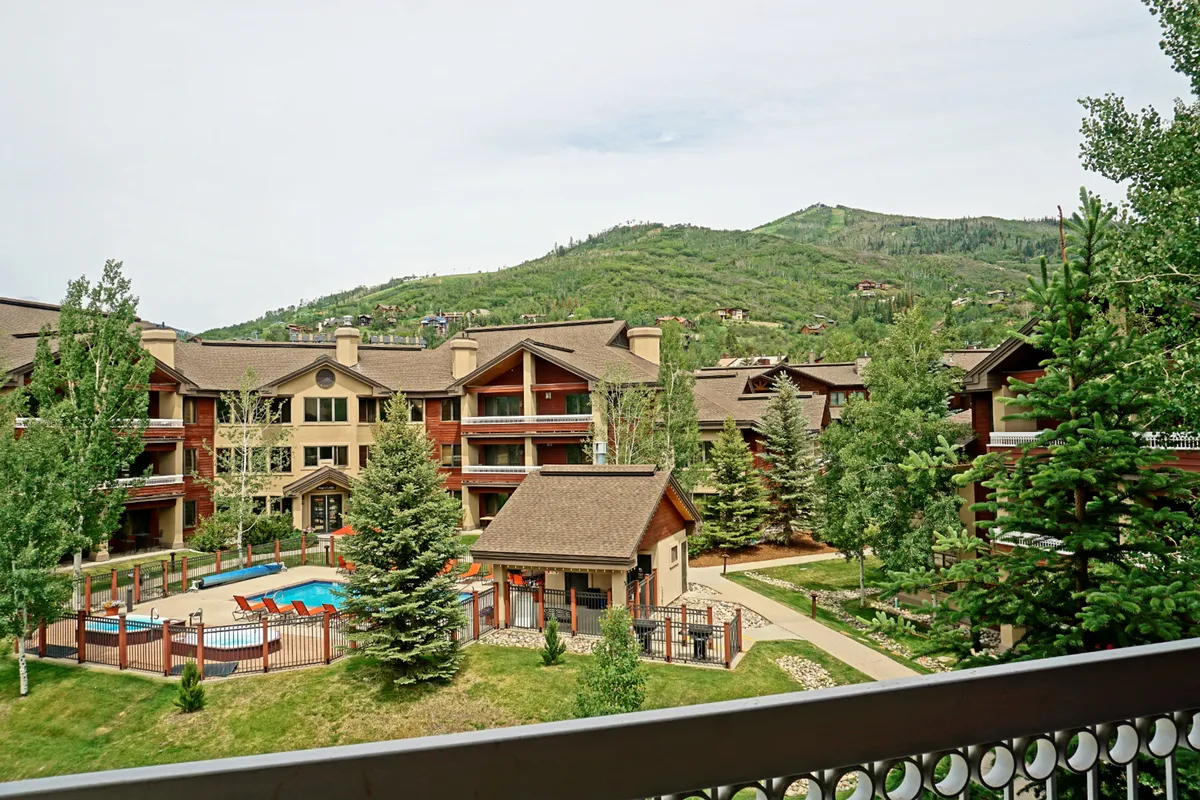 An exterior shot capturing the swimming pool, manicured gardens, and mountain backdrop, with a clear view of balconies overlooking these beautiful surroundings. The image hints at the experience of enjoying sunset views or morning coffee from the balcony, with a direct connection to the landscape and resort amenities.