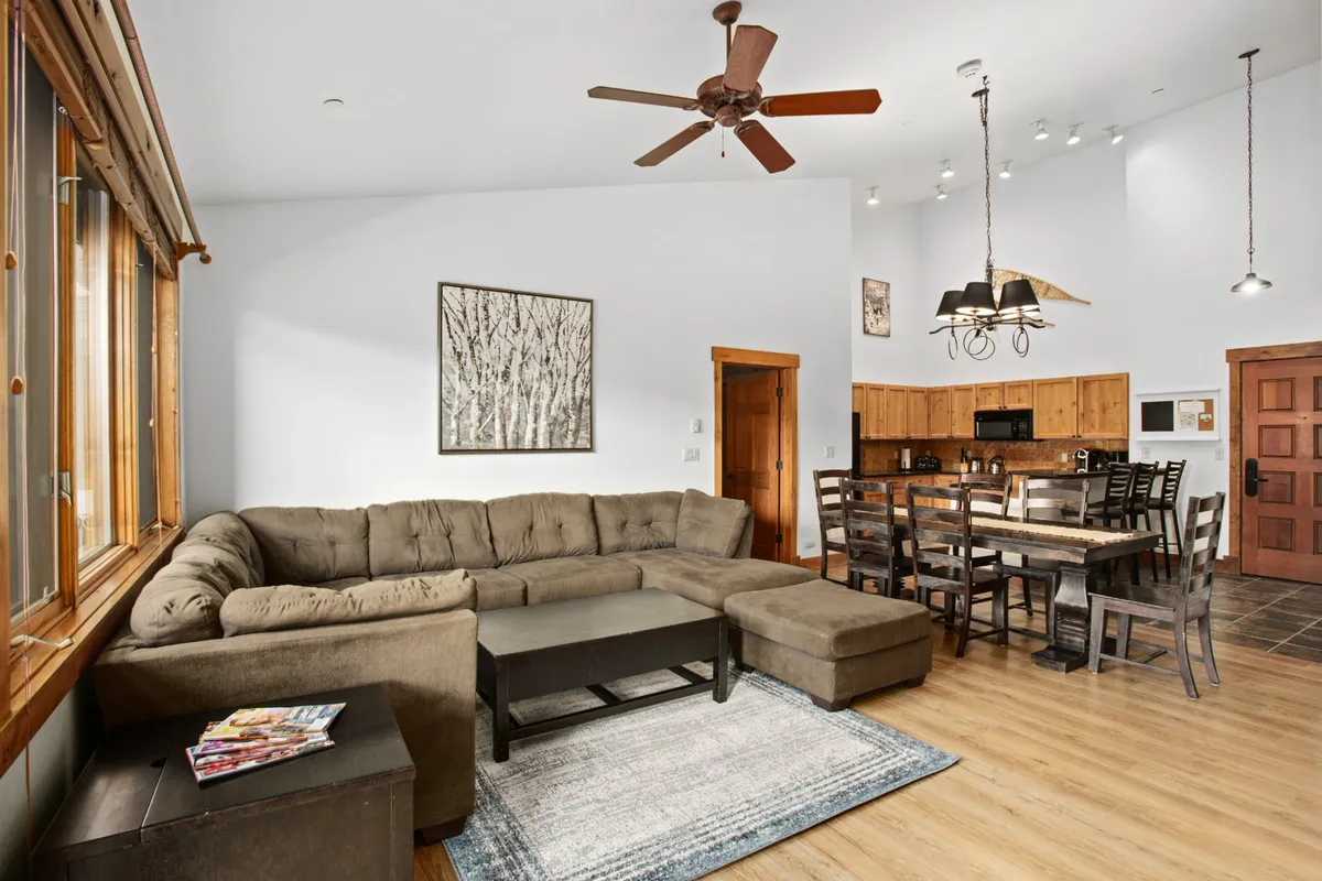 The image presents a large sectional sofa, a dining table, and wall artwork, all elements that contribute to an inviting and versatile living space ideal for family gatherings, lounging, and shared activities.