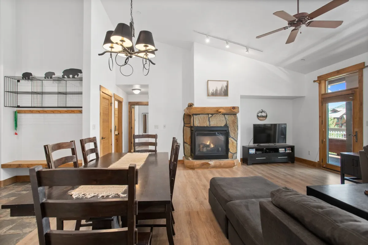 A harmonious view of the dining area, fireplace, comfortable sofa, and a striking lighting fixture above. The arrangement feels intimate, yet spacious enough for group dinners, game nights, or lounging by the fire.