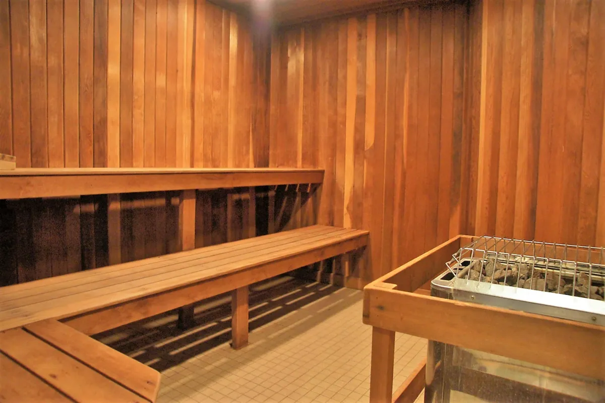 A serene interior sauna with wooden benches, a stone heater, and warm wood paneling. The tranquil atmosphere invites guests to unwind and socialize in a peaceful setting.