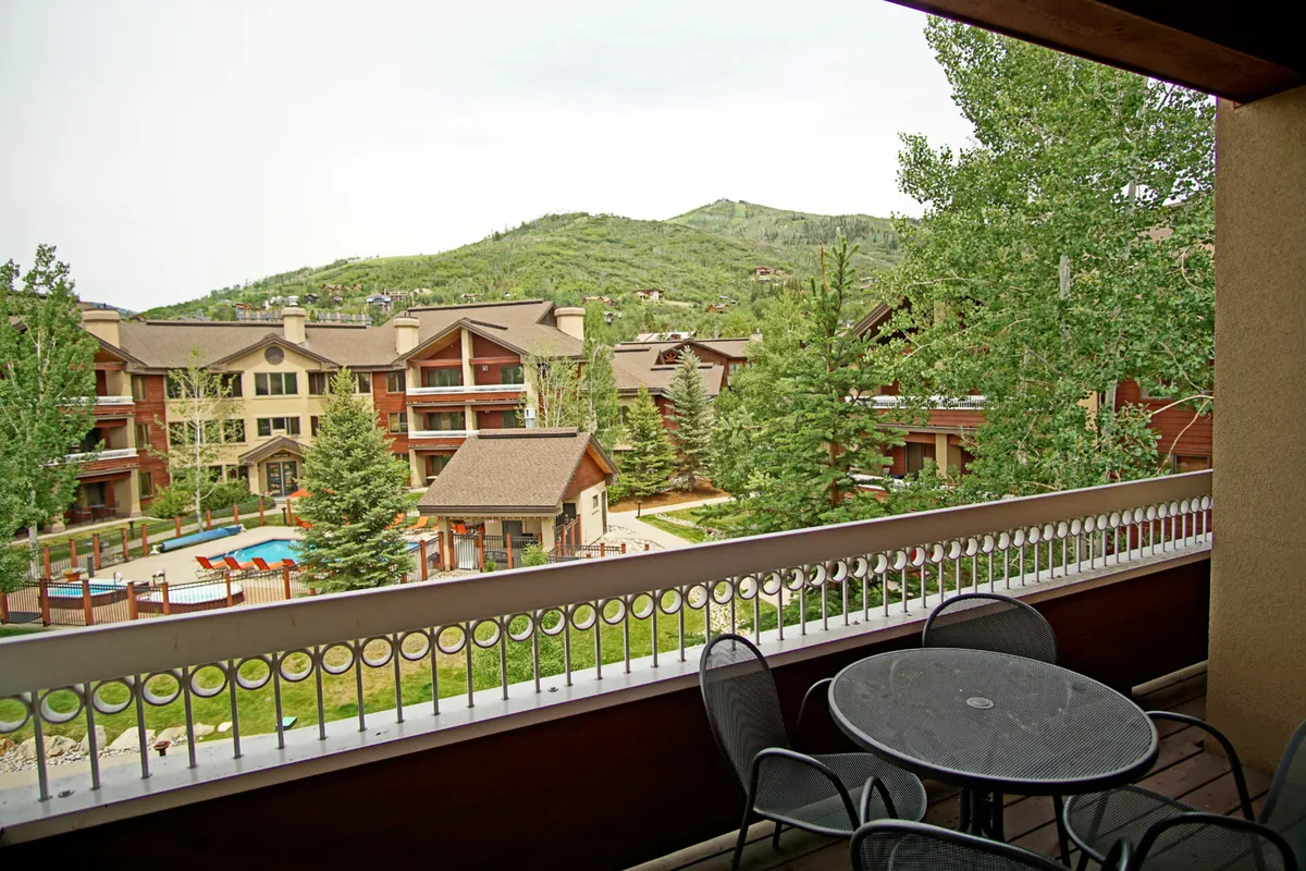 This image showcases a spacious balcony furnished with seating, offering a sweeping view of the pool area, surrounding trees, and distant mountains. The scene exudes tranquility and highlights the balcony as a prime spot for relaxing outdoors while enjoying Colorado’s natural beauty.