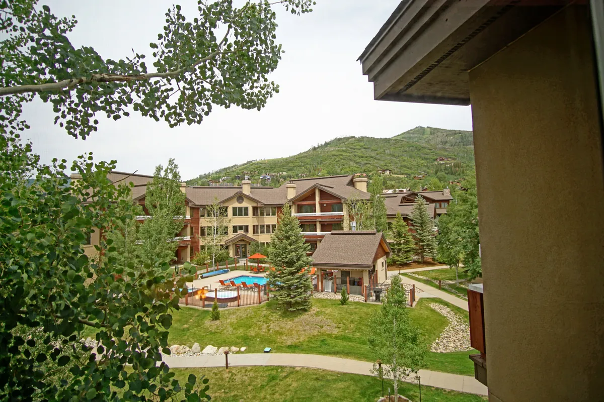 An exterior shot featuring a sparkling swimming pool, lush landscaping, and distinctive wooden architecture, all set against a dramatic mountain backdrop. The space is inviting for relaxation and socializing after outdoor adventures.