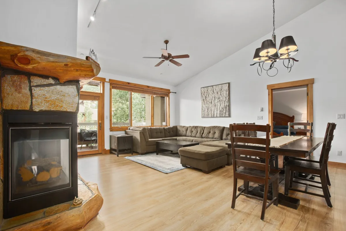 This image showcases an expansive interior featuring a cozy living area with a plush sofa, a gas fireplace, large windows flooding the space with light, and an adjacent dining table. The arrangement emphasizes togetherness—perfect for family gatherings, dining, or relaxing by the fire.