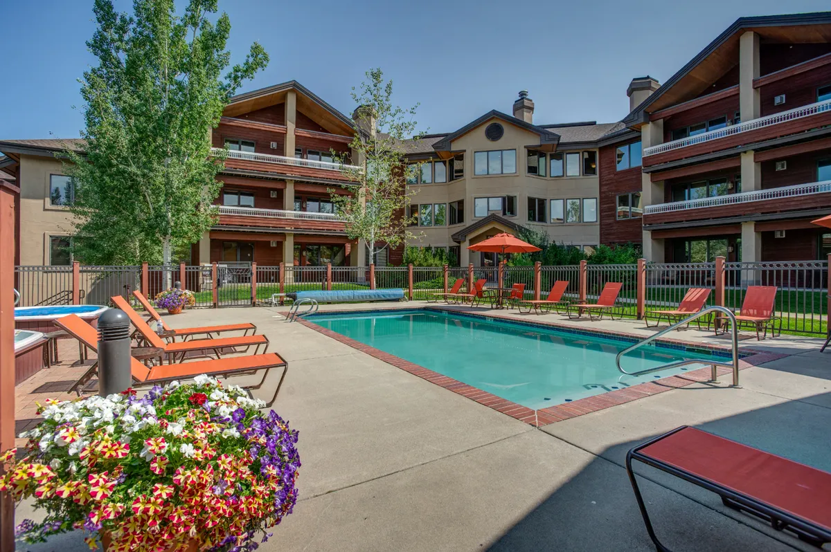 A spacious outdoor pool area surrounded by lounge chairs, flowerbeds, and the property buildings. The scene feels lively yet relaxed, with spots for swimming, sunbathing, or socializing with fellow guests.