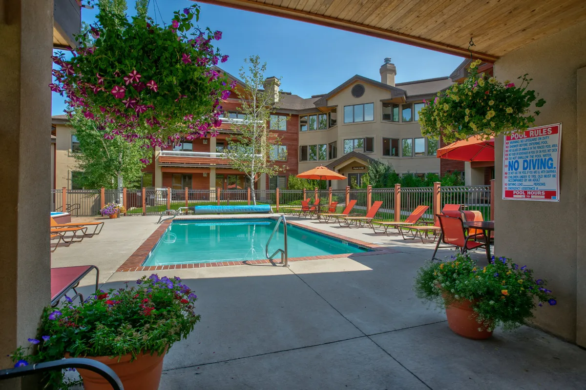 The photo features a sparkling swimming pool surrounded by lounge chairs, hanging flower pots, and the building facade, capturing the resort's communal and recreational amenities. The cheerful mood and outdoor setting suggest summer fun for all ages, perfectly aligning with the summer family activities highlighted in the text.
