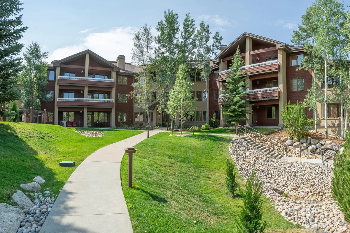 A view of the building's facade with a green lawn, walking path, and a rock garden, this photo highlights the inviting walkability of the property. The landscaped grounds suggest a family-friendly environment suitable for strolls, play, or relaxing between activities.