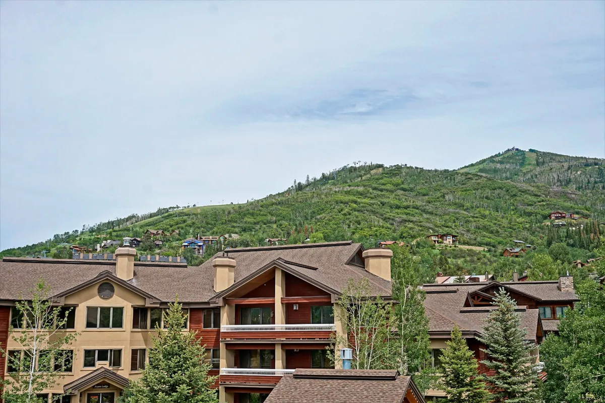 This image captures a wide mountain landscape set behind residential buildings and mature trees, emphasizing the natural setting and proximity to outdoor activities. The open, serene environment hints at both winter and summer experiences families can enjoy just outside the condo.